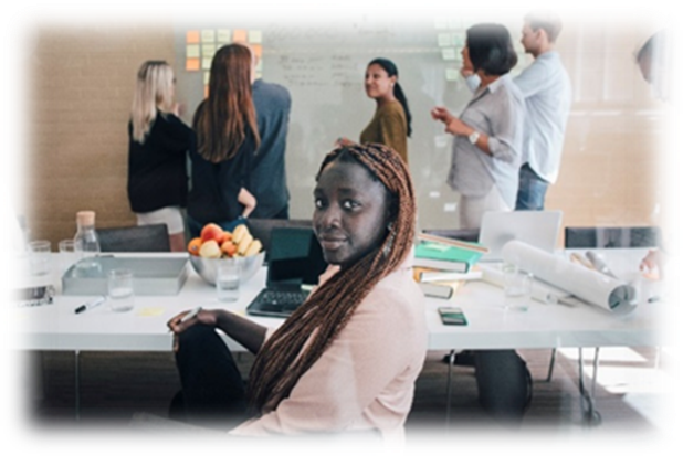 A decorative image chosen to represent a module leader. She sits in the foreground of a busy planning scene in profile, turning her head towards you and smiling. Behind her is a table filled with paper, cards and a bowl of fresh fruit. In the background, six people in business wear stand deep in conversation near a floor-to-ceiling white board.