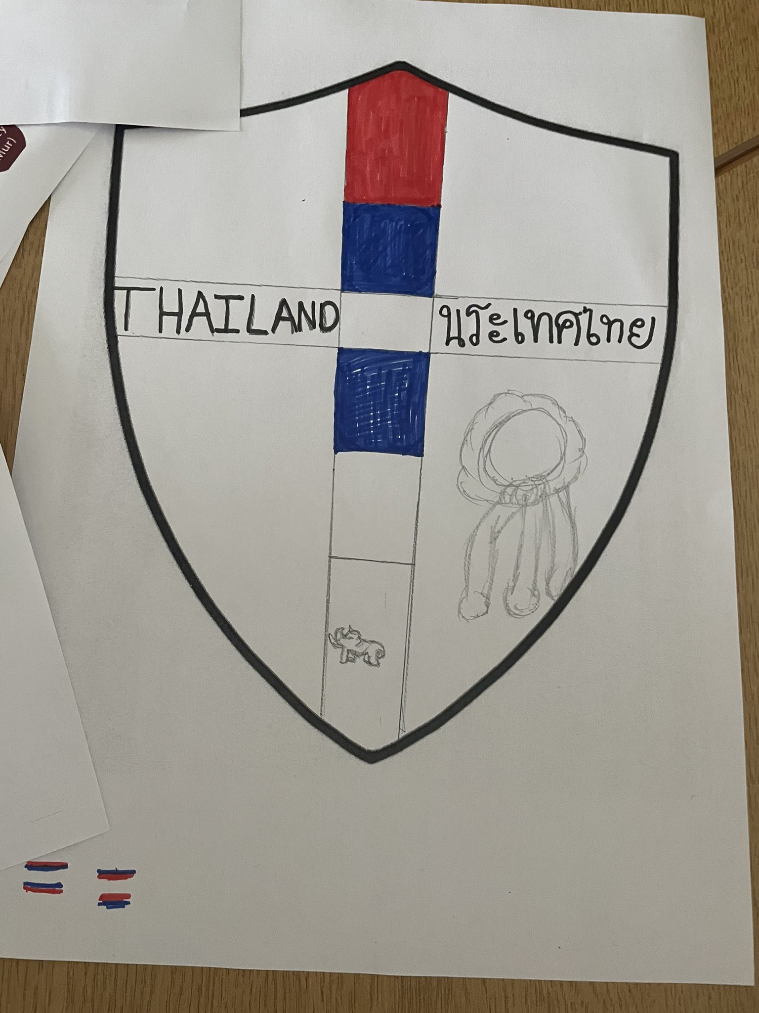A shield with a cross through the middle. Thailand is written in English and Thai  across the middle with a flower in the lower quarter