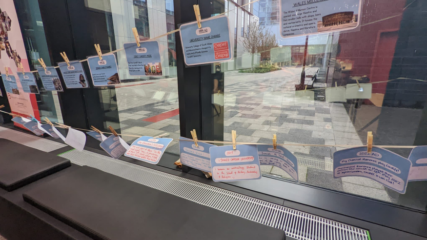 Washing line hung across a large window with pegs holding cards describing various historical events in Cardiff.